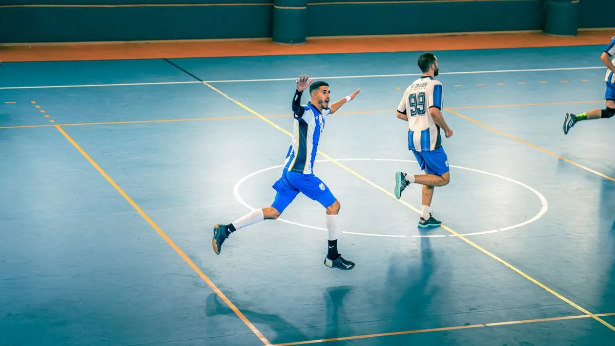 Partido de fútbol sala en pista cubierta con jugadores corriendo hacia el círculo central