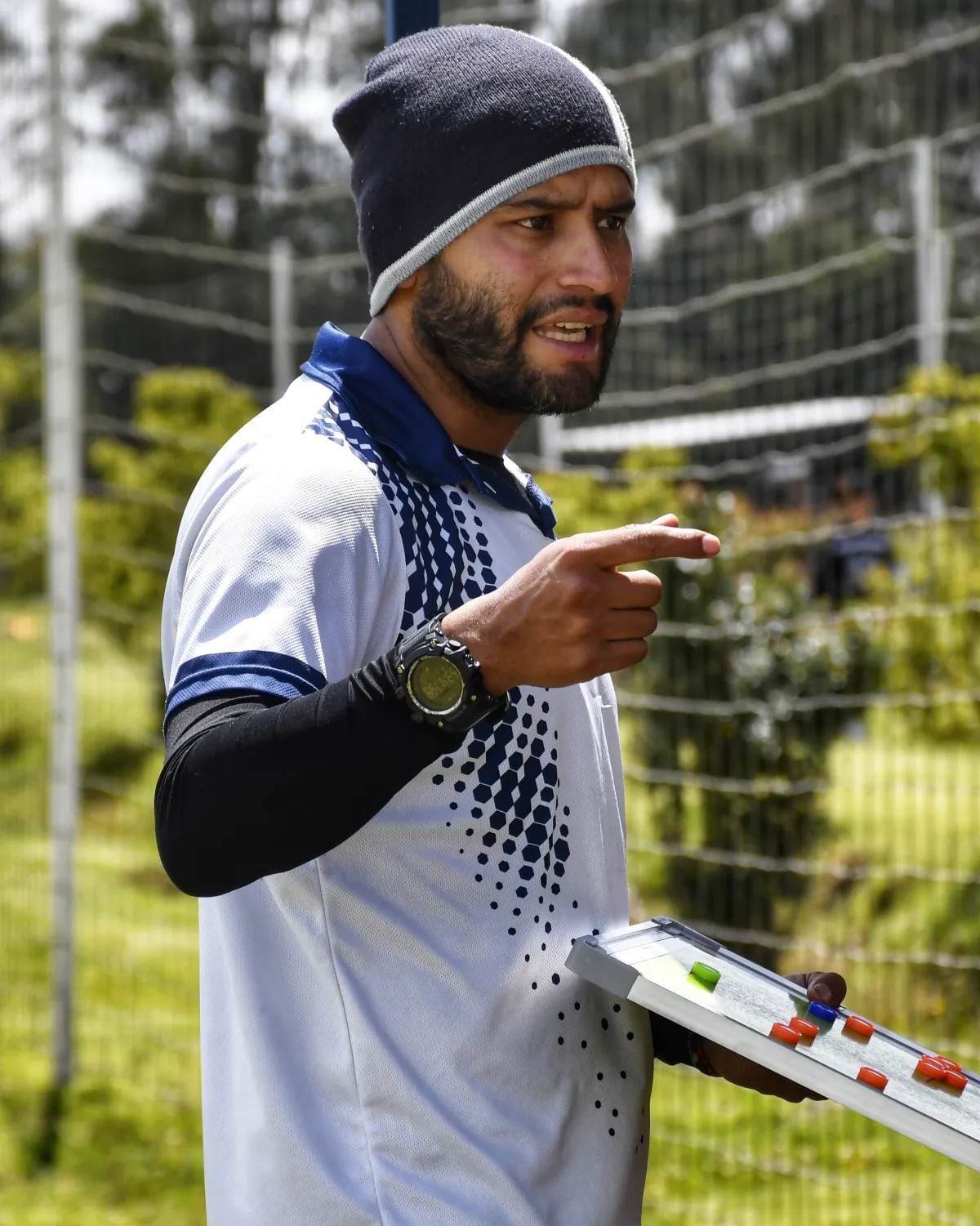 Coach pointing while holding a tactics board on the pitch